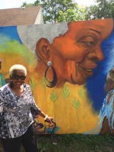 An old woman taking a picture in front of a wall painting