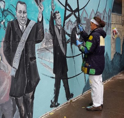 A woman in a black jacket painting a wall