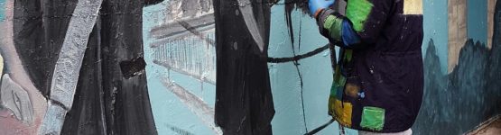 A woman in a black jacket painting a wall