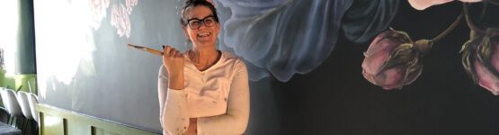 A woman standing in front of a mural painted with flowers.
