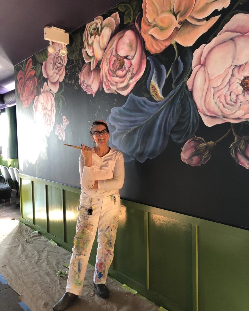 A woman standing in front of a mural painted with flowers.